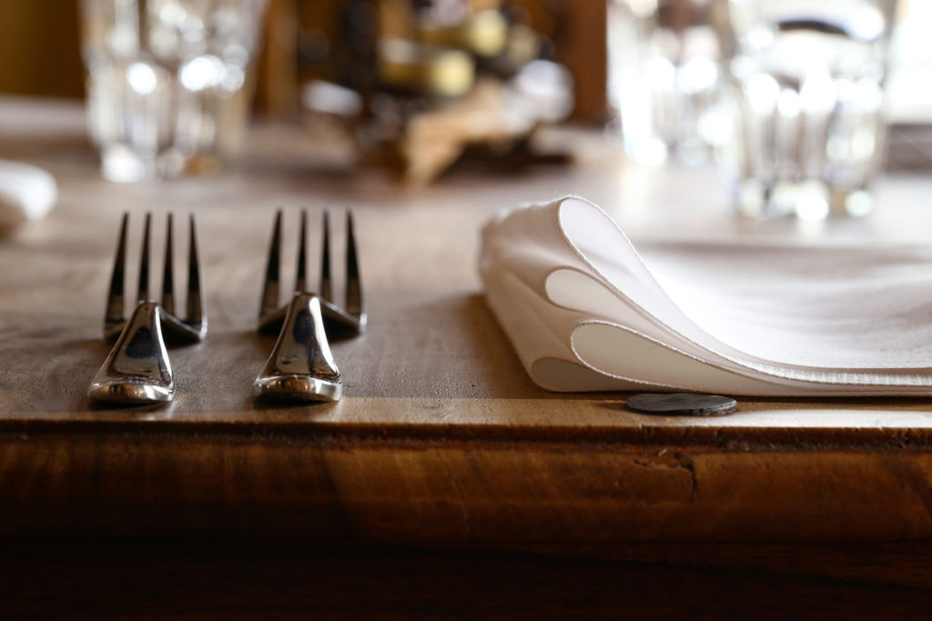 a picture of a place setting at a restaurant with two forks on the left hand side and a linen napkin on the wooden table. Glasses are sparkling in the background. This image represents the Restaurants Brighton Gift Vouchers page where gift vouchers can be redeemed across multiple locations in Brighton, Hove and Sussex.
