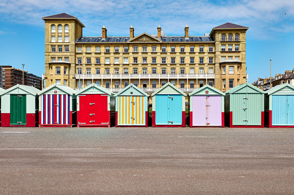 Colourful Brighton beach huts in a row with a big building in the background.