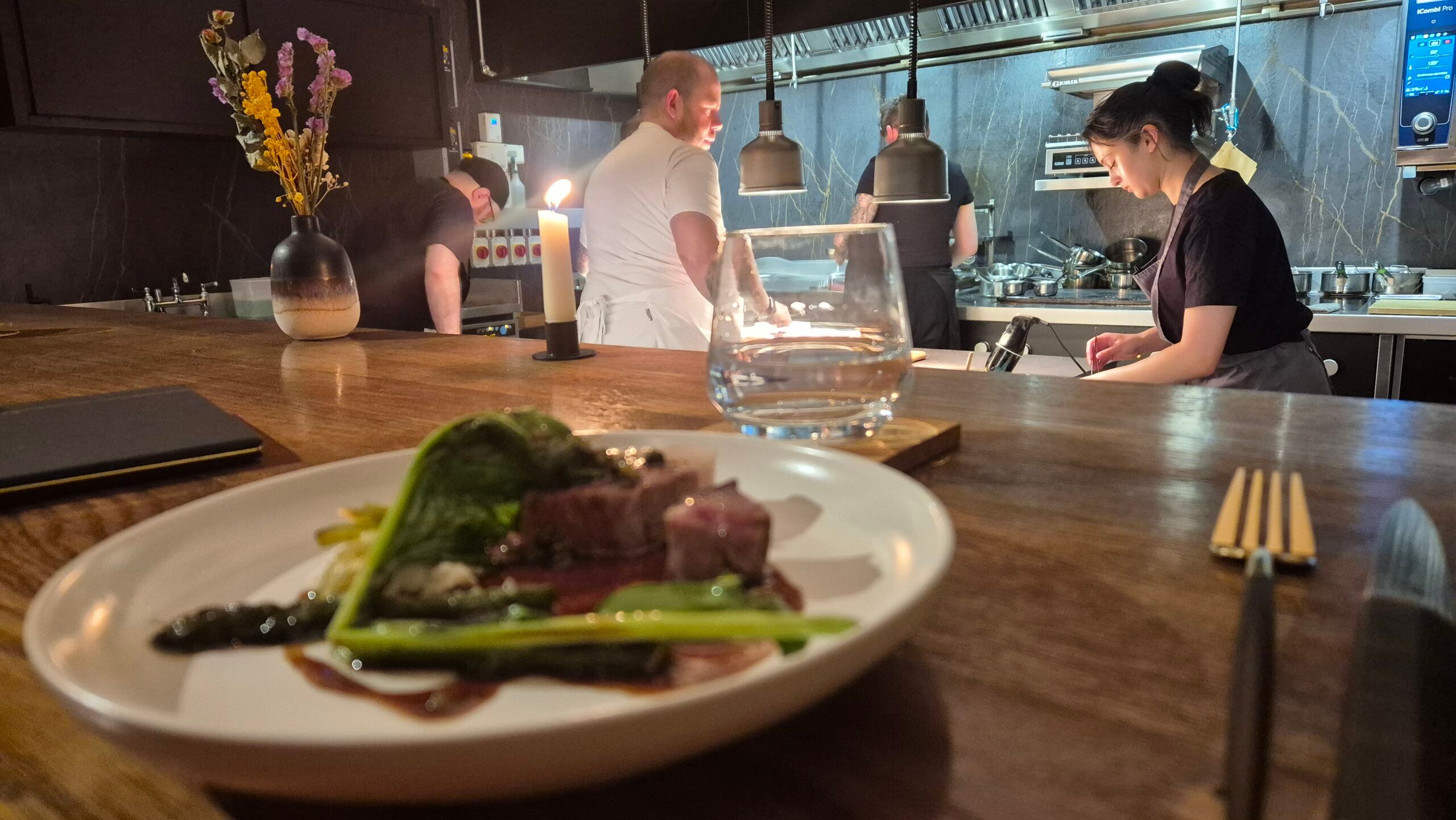 spring lambs served with veggies on the white plate with the view of two chefs in kitchen