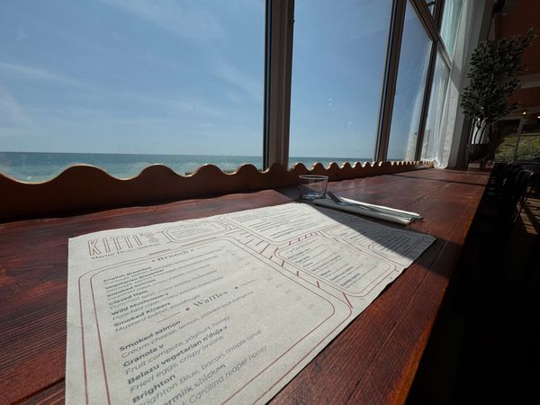 a cafe menu on a long table that overlooks the sea. the sky is blue.