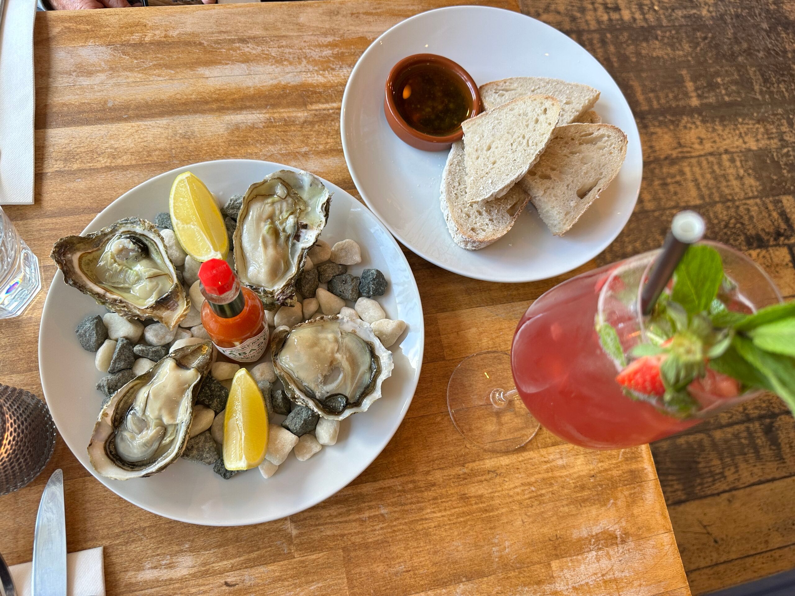 over head shot of the oysters served in white plate with bread and sauce on the side, and glass of red drink