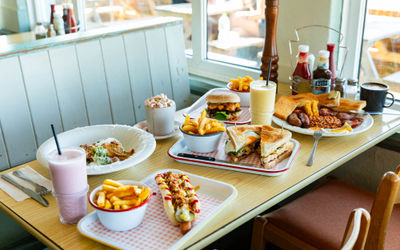 window table laid out with multiple dishes including toasts with chips, burger with chops, few drinks and sauces