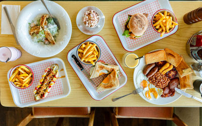 over head shot of the wooden table at Roedean Cafe populated with various dishes including full english breakfast, burgers and chips, toasts and chips, coffee and smoothies