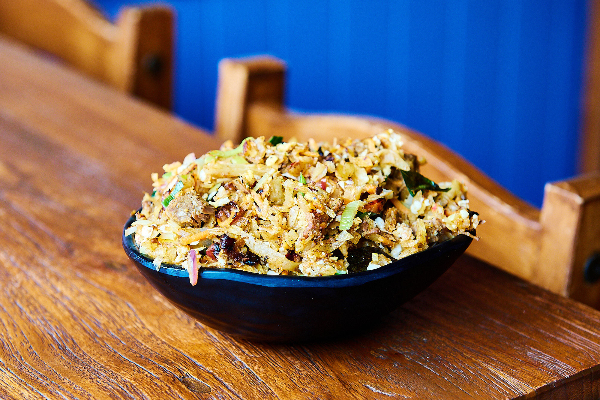 A bowl of Kothu chopped roti with mixed veg and beef on a wooden table.