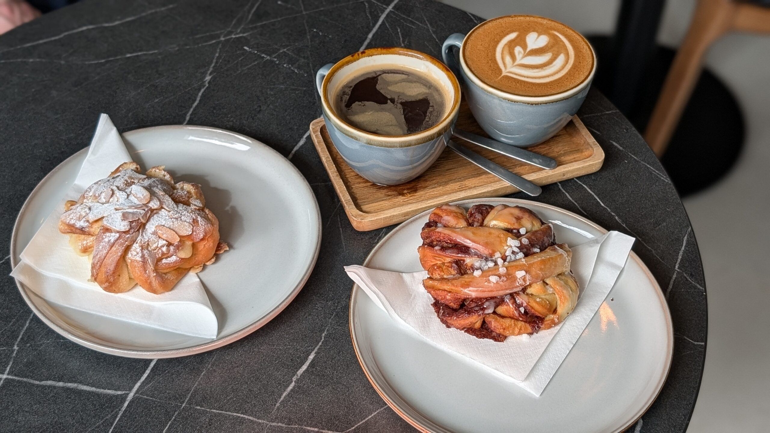 Americano and flat white coffee served on wooden plate and with two pastries