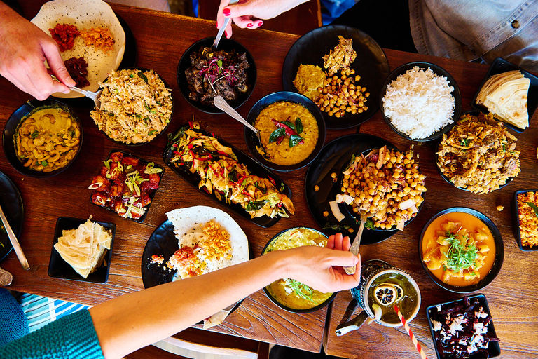 A feast of Sri Lankan street food with lots of bowls and plates of food and people's hands reaching over.