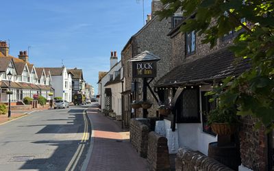 a road with the village pub called The Duck Inn on the right hand side of the street. The sky is blue, the building is old.