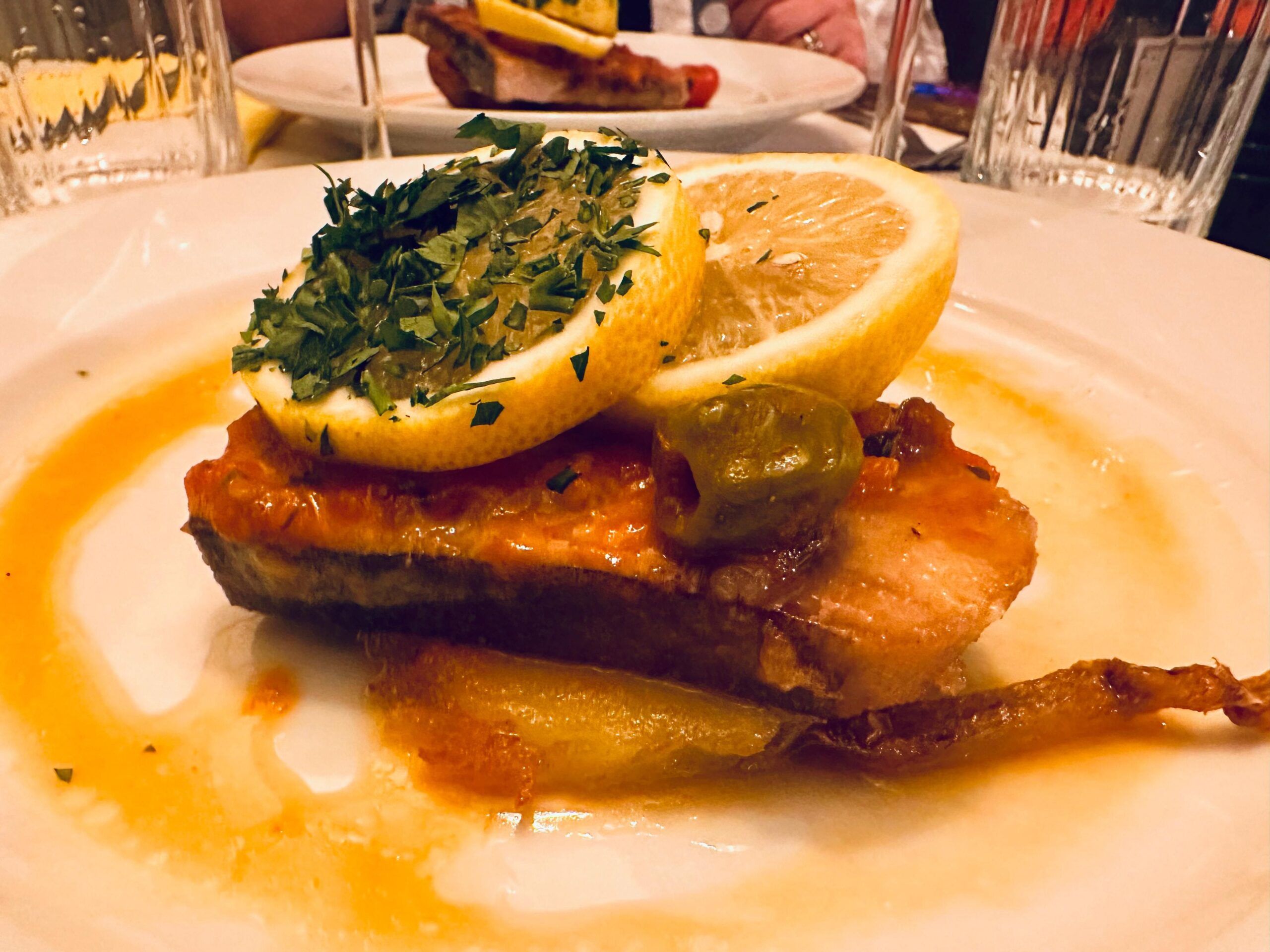 meaty swordfish steak served on a layer of fondant potatoes and topped with olives, capers, cherry tomatoes, onion and fresh parsley