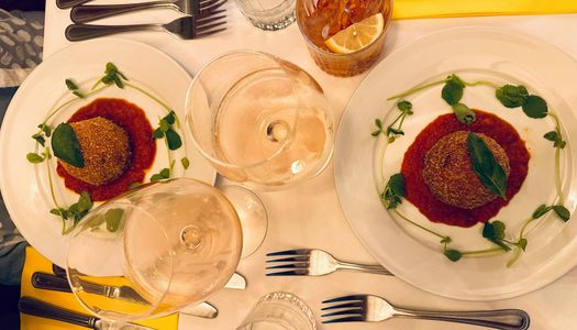 over head shot of the two plates with giant rich arancino, coated with breadcrumbs and filled with ragù, buffalo mozzarella and peas