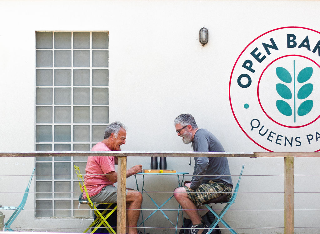 two gents playing a board game outside the Open Bakery in Queens park