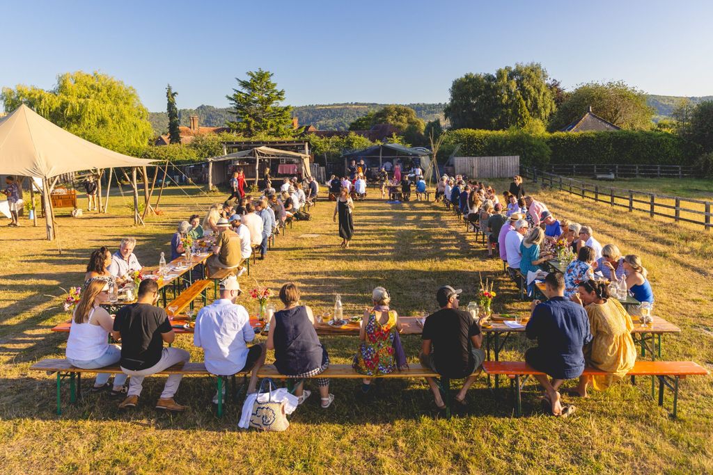 woodfire camping feast - long tables and lots of people sitting and enjoying their food on the camping site