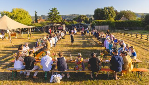 woodfire camping feast - long tables and lots of people sitting and enjoying their food on the camping site