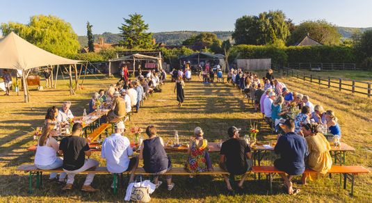 woodfire camping feast - long tables and lots of people sitting and enjoying their food on the camping site