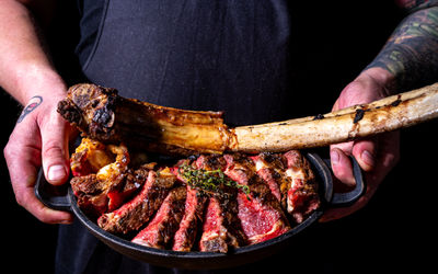 stylish steakhouse and cocktail bar on Church Road, Hove, featuring a modern façade and terrace under moody lighting. Picture of chef holding T Bone steak