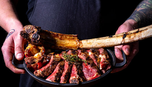 stylish steakhouse and cocktail bar on Church Road, Hove, featuring a modern façade and terrace under moody lighting. Picture of chef holding T Bone steak