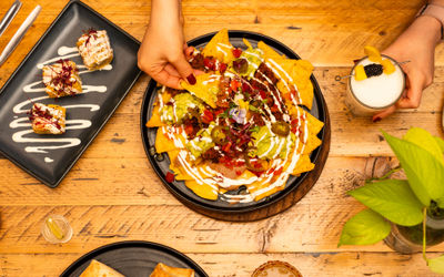 Nachos served on a plate with garnishes and a person picking up a tortilla chip