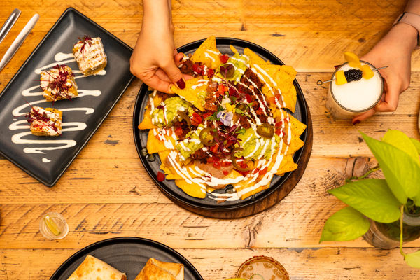 Nachos served on a plate with garnishes and a person picking up a tortilla chip