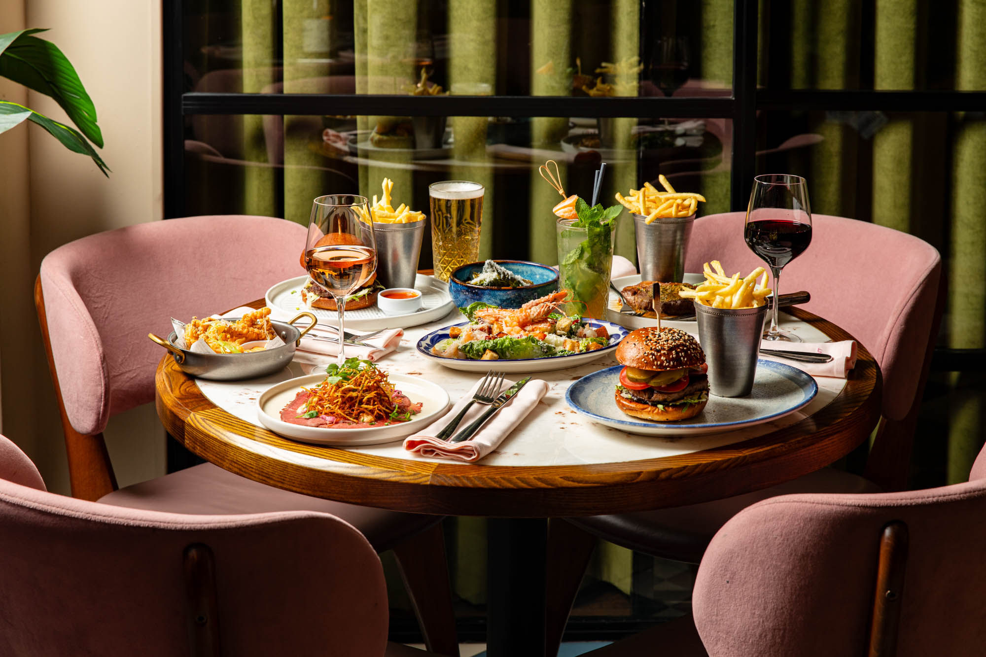 side shot of the brown wooden table at Burger and Lobster laid out with couple of dishes including burgers, steak, chips and more. 