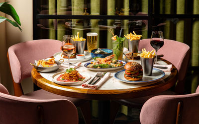 side shot of the brown wooden table at Burger and Lobster laid out with couple of dishes including burgers, steak, chips and more.