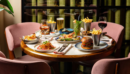 side shot of the brown wooden table at Burger and Lobster laid out with couple of dishes including burgers, steak, chips and more.