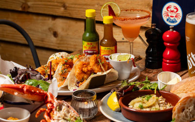 table laid out with various dishes including seafood tacos, lobster, two sauces and cocktails