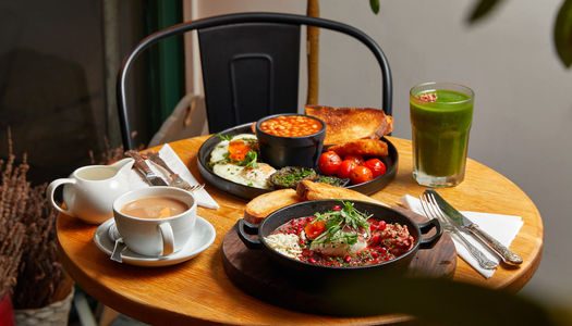 table laid out with breakfast dishes including full englihs, coffee, green smoothie
