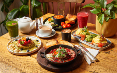side shot of the table laid out with various dishes including full english, pancakes, toast, coffee, tea, smoothie