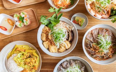 over head shot of the wooden brown table populated with various Vietnamese dishes