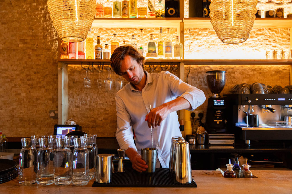 Alistair stirring a cocktail at Apiary with carafes of water on the side and a coffee machine in the background.