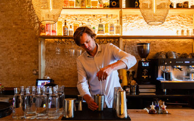 Alistair stirring a cocktail at Apiary with carafes of water on the side and a coffee machine in the background.