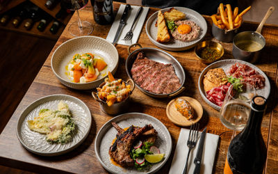 wooden table at Carne Hove laid out with six delicious dishes with sides, including steak, fries, charcuterie, tartare and more.