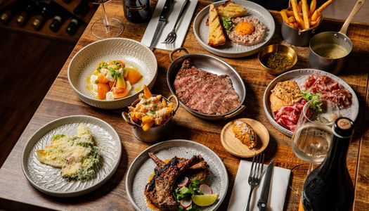 wooden table at Carne Hove laid out with six delicious dishes with sides, including steak, fries, charcuterie, tartare and more.