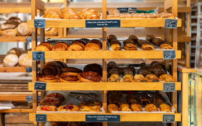 A wooden bakery display full of fresh bakes. Each shelf has a selection of freshly baked pastries. It looks inviting and delicious.