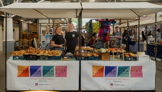 A colourful display of Swedish buns and pastries from Fika Bakery at Brighton Open Market, arranged on trays against a vibrant background—showcasing cinnamon buns, cardamom swirls, croissants, and other freshly baked Scandinavian treats.