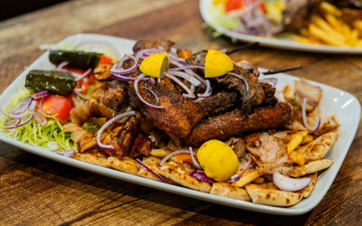 Greek mixed grill platter at Parthenon Gyros in Brighton, served with pita bread, fries, salad, lemon wedges, and topped with sliced red onions."