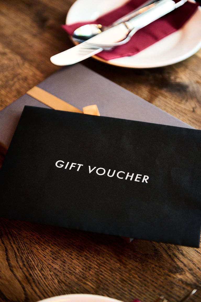A black envelope on top of a gift box on a wooden table with a side plate in the background.