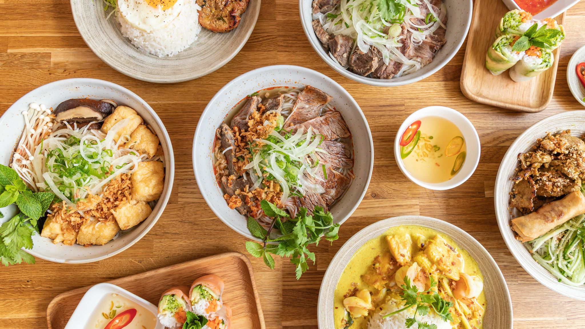 over head shot of the wooden brown table populated with various Vietnamese dishes