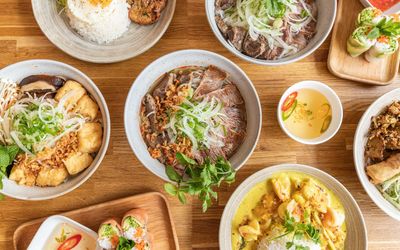 over head shot of the wooden brown table populated with various Vietnamese dishes