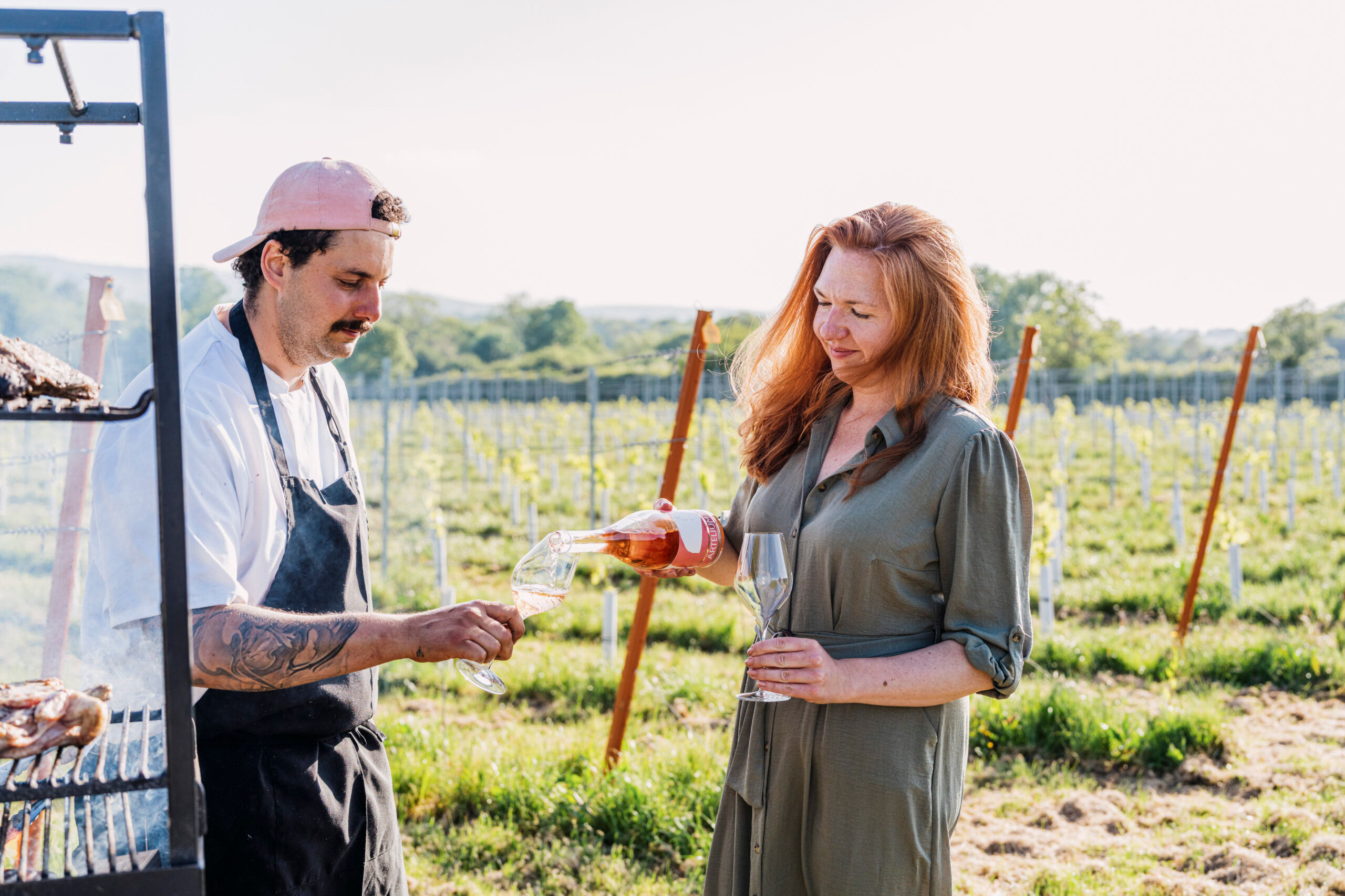 Chef being poured a glass of wine, with vineyard backdrop