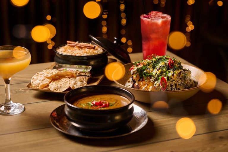 A table full of plates of curry, rice, cocktails and twinkly lights.