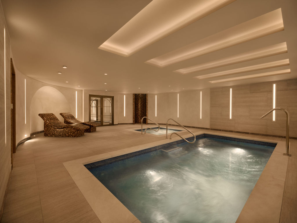 Indoor spa pool area with bubbling water, sleek mosaic lounge chairs, and soft ambient lighting in a modern well-appointed room.