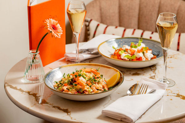 a small table is set with 2 bowls of healthy fresh food. A fresh flower sits in a small vase and 2 glasses of fizz suggests this meal is a real treat.