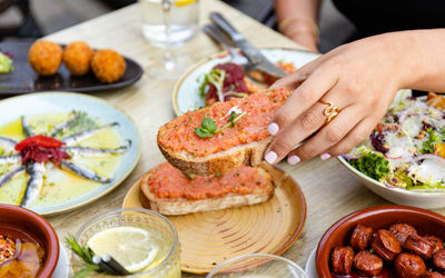 A table is full of tapas and a causcasian had reaches out for a slice of bruschetta. The food on the table looks tasty.