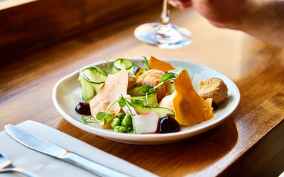 A side shot of a plate of vibrant ingredients with a glass of wine being picked up in the background at Fourth and Church in Hove