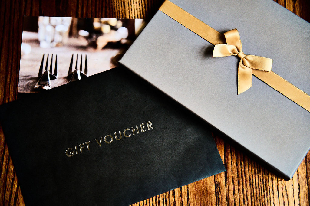 A grey box with a gold ribbon for a gift voucher in a black envelope.