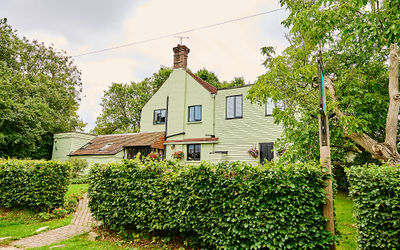 A wide exterior shot of A large bed with white and blue bedding at The Jolly Sportsman Pub in Sussex with leafy trees surrounding the building.
