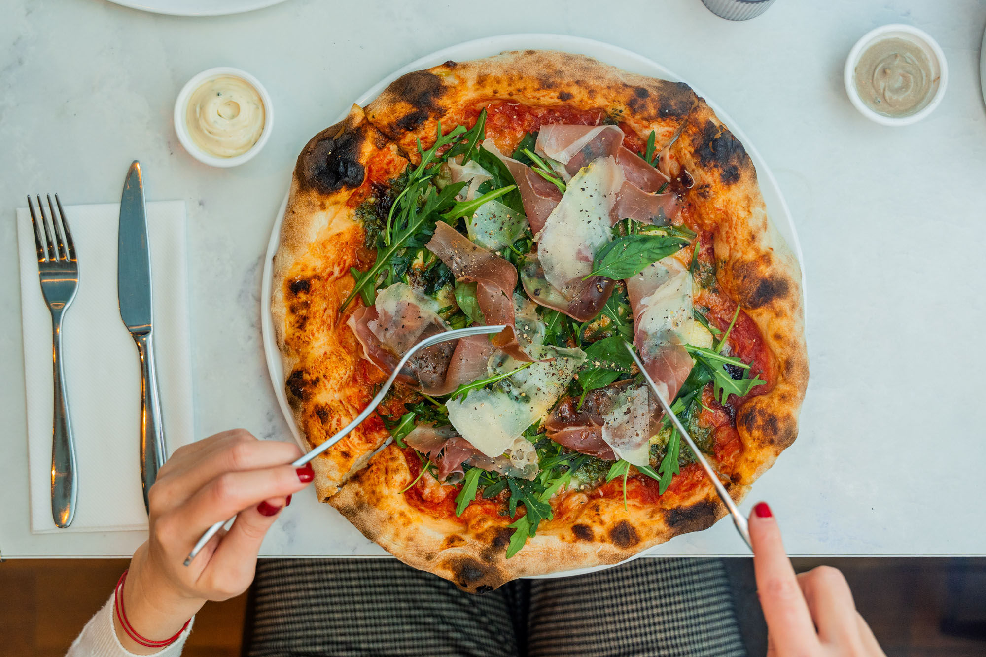 over head shot of the hands using knife and fork to cut pizza