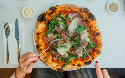 over head shot of the hands using knife and fork to cut pizza