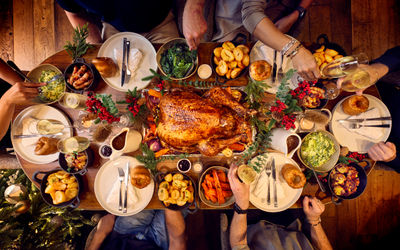 A dining table for 6 is set for christmas. The photography is from above and shows a whole festive spread with a glazed turkey being in the centre of the table. Places are set with white plates and silver cutlery. Surrounding the turkey are bowls of trimmings from brussel sprouts, carrots and roast potatoes. it looks like a proper feast.