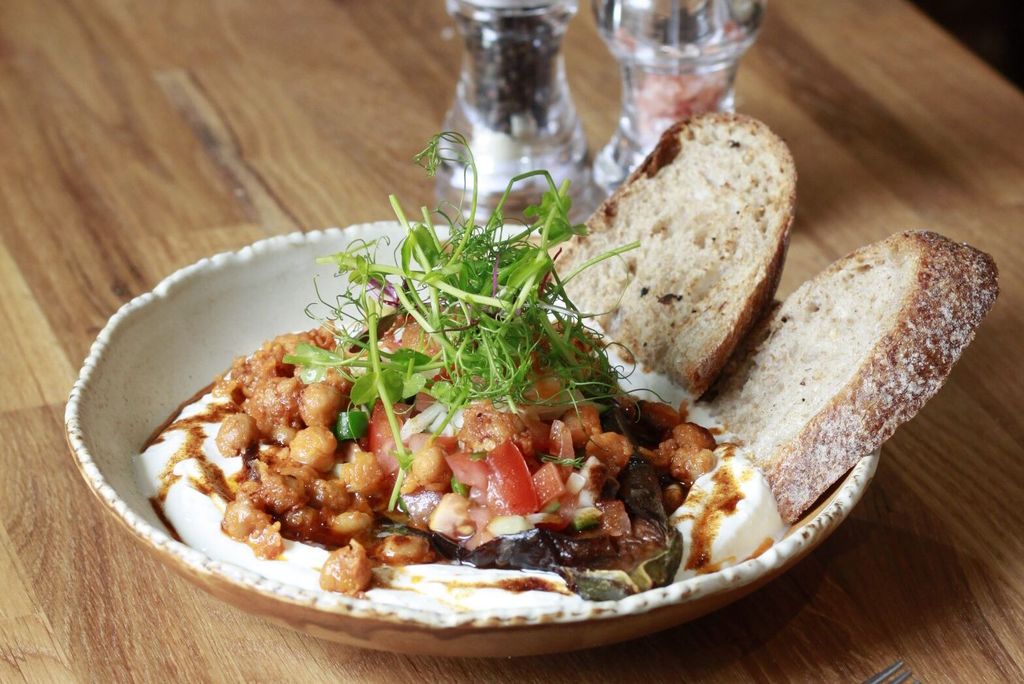 A Mediterranean-style brunch dish with chickpeas, tomatoes and herbs served over creamy yoghurt, with slices of rustic sourdough bread. Turkish influences